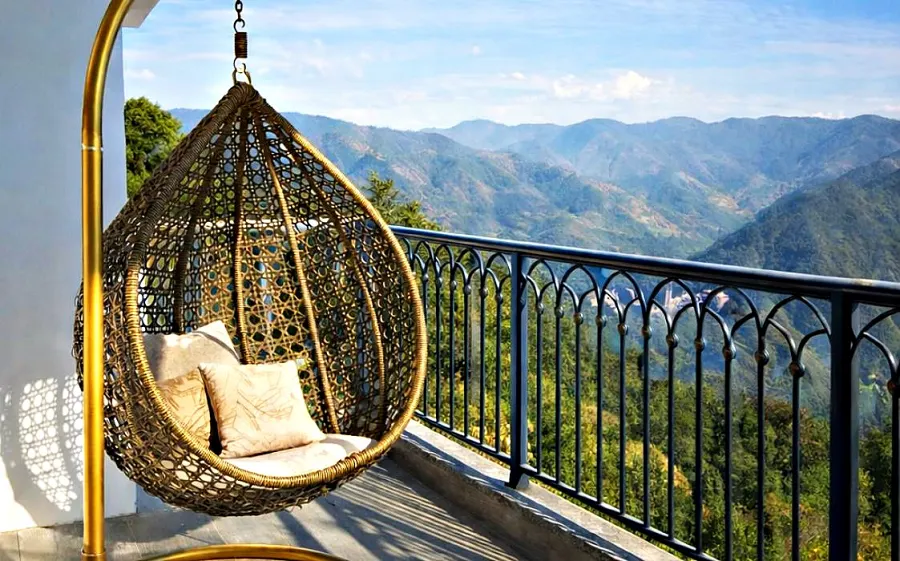 Rattan hanging chair on a private balcony at Sukhvasa Villas, looking out over the layered Himalayan valley