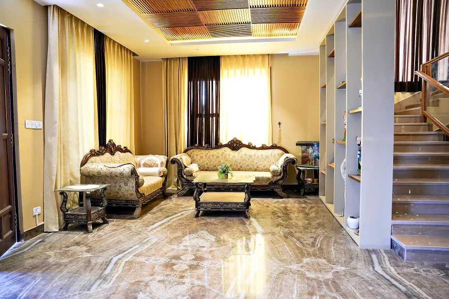 The main living hall with carved cream and gold sofas, a marble floor and the staircase rising behind