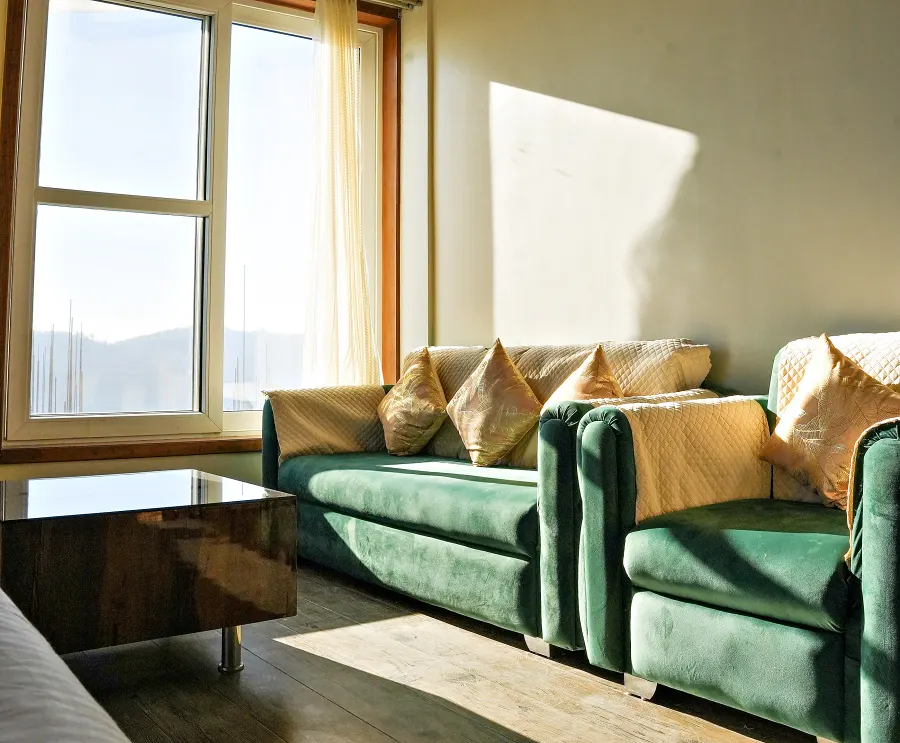 Green velvet sofas arranged to face the tall windows and the light off the valley