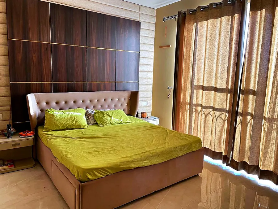 Deluxe bedroom with an olive bed, timber headboard wall and floor-length curtains